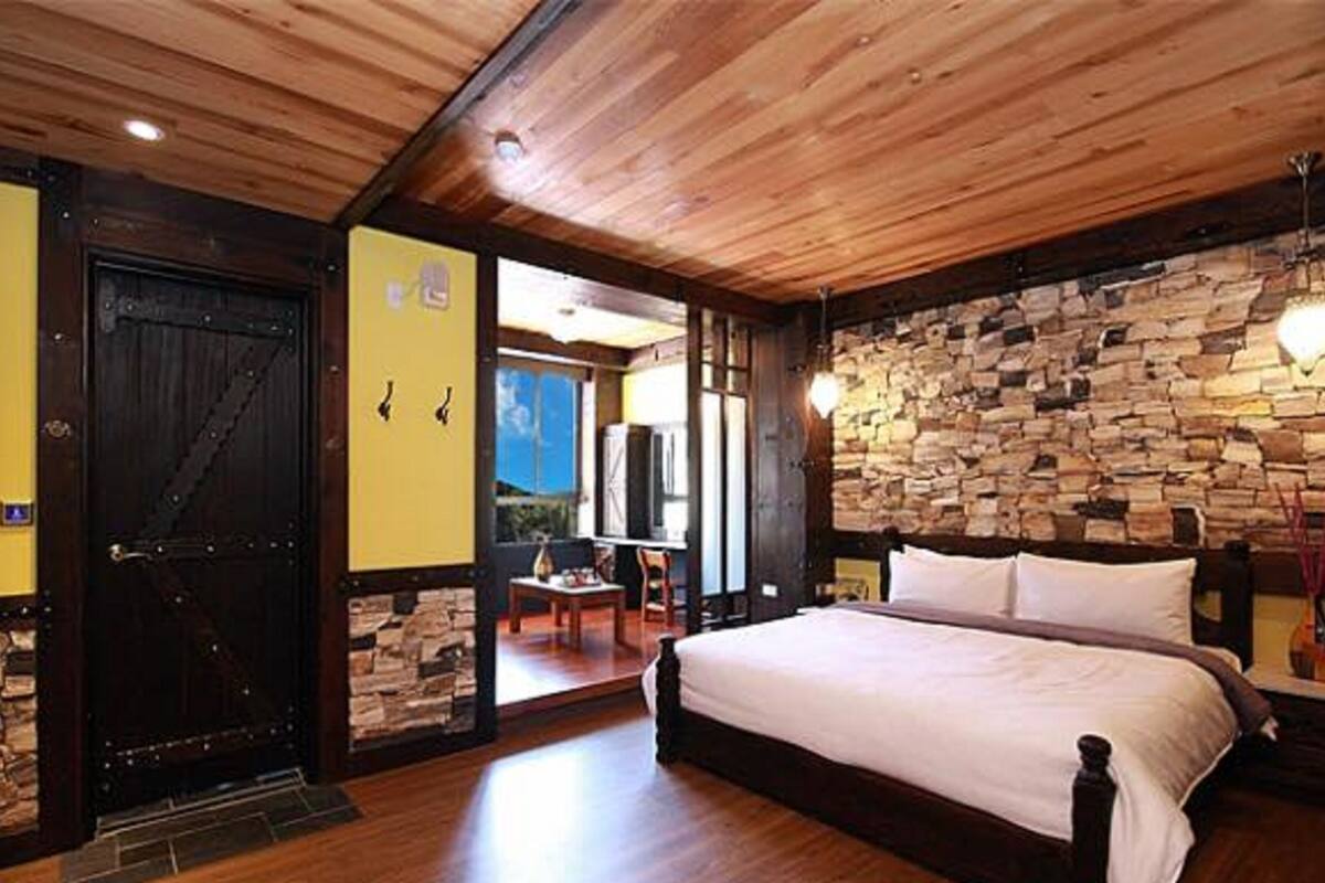 Un dormitorio con pared de piedra, techo de madera y cama con ropa de cama blanca.