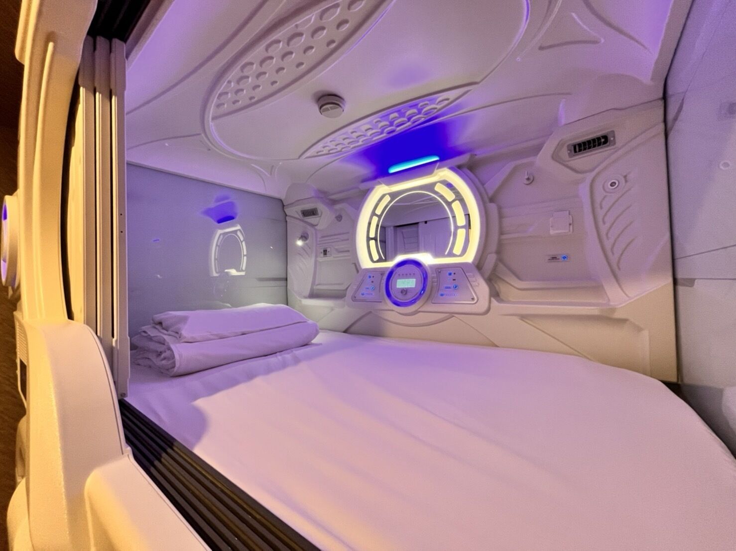 A room with a bed, a control panel, and a circular light fixture.