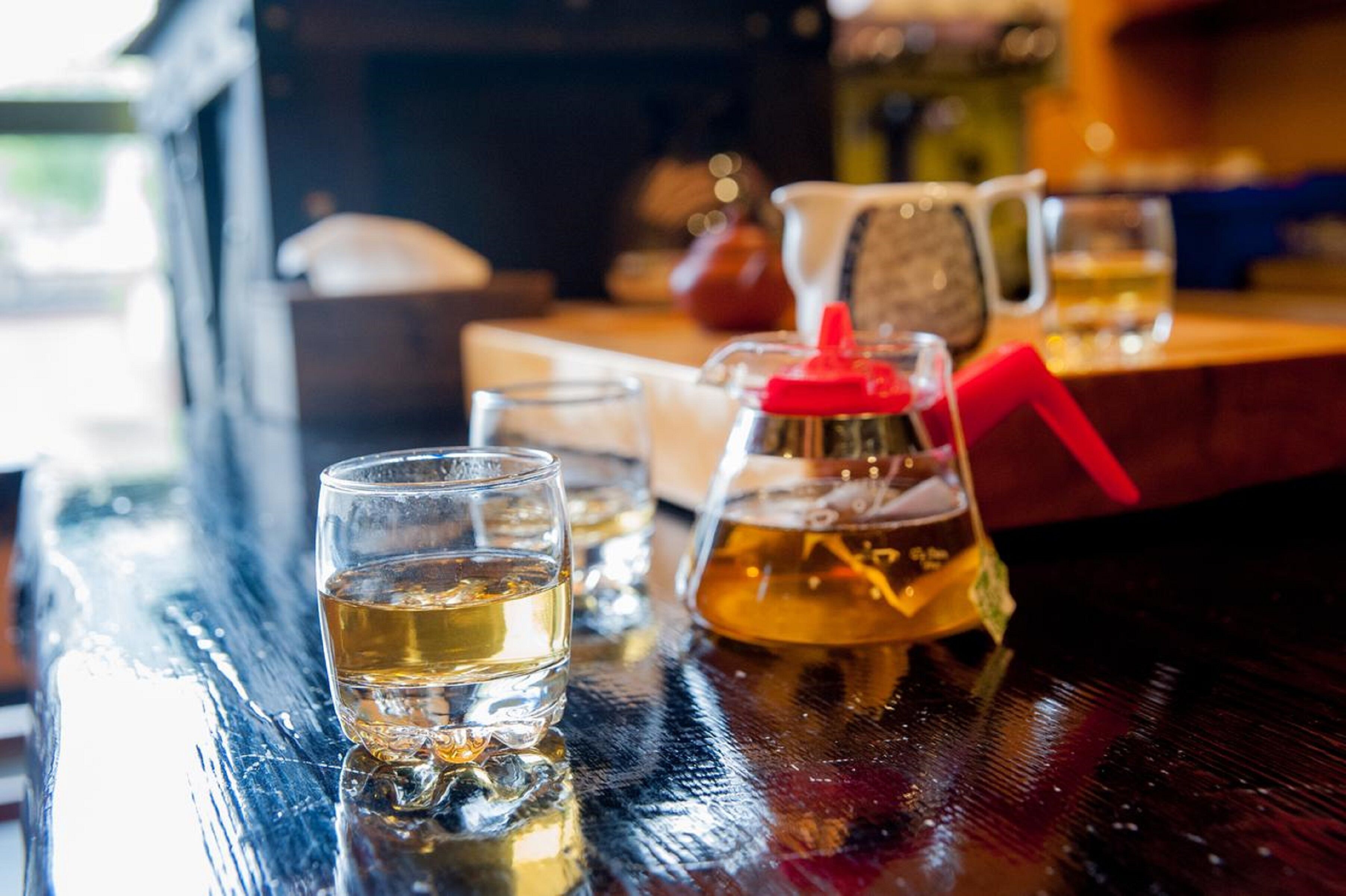 A bar setting with glasses of a golden beverage, a pitcher with a red lid, and a glass pitcher on a wooden surface.