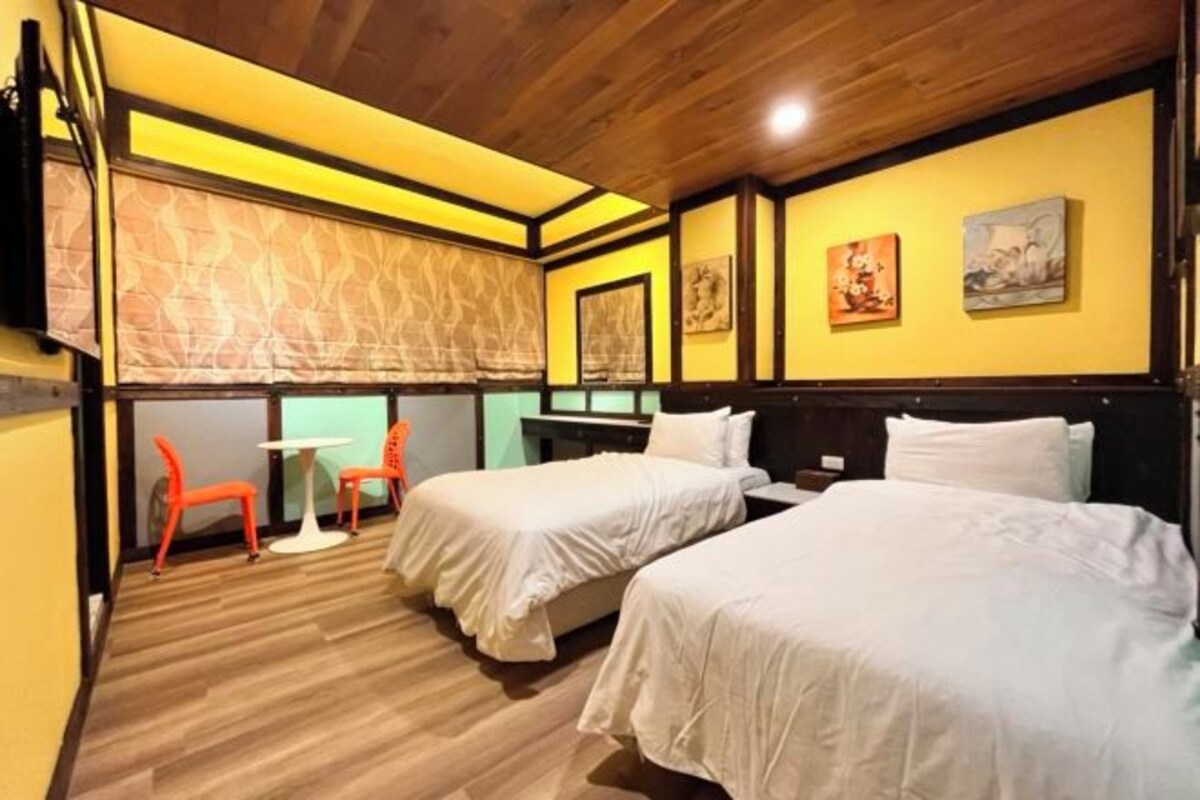A hotel room with two beds, a small table, and two orange chairs.
