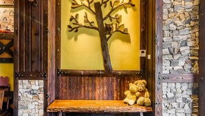 A wooden bench with a stone wall backdrop, a tree sculpture, and a teddy bear.