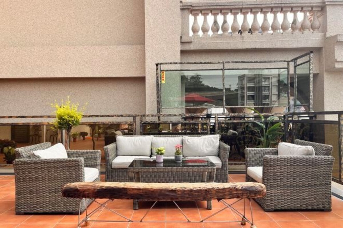 A terrace with wicker furniture, a glass balustrade, and a view of the cityscape.