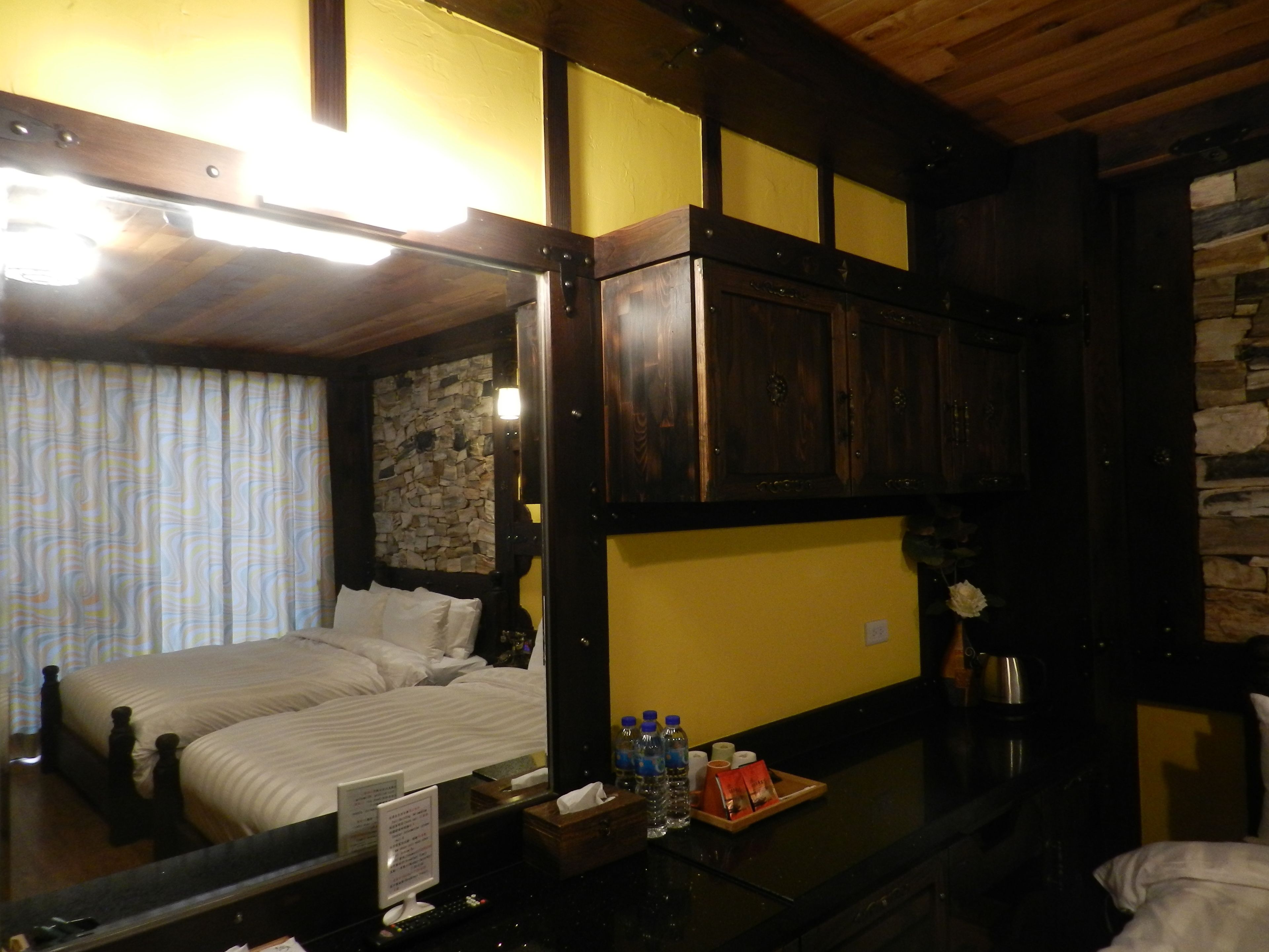 Habitación de hotel con cama, espejo, mueble de madera, pared de piedra y una pequeña mesa con artículos de aseo.