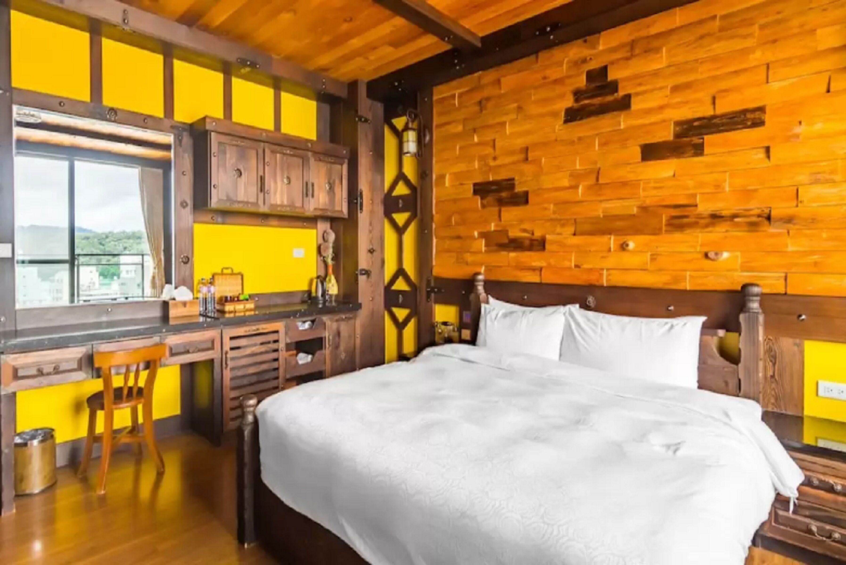 Une chambre à coucher avec une tête de lit en bois, un grand lit, un bureau avec une chaise et une fenêtre donnant sur un beau paysage.