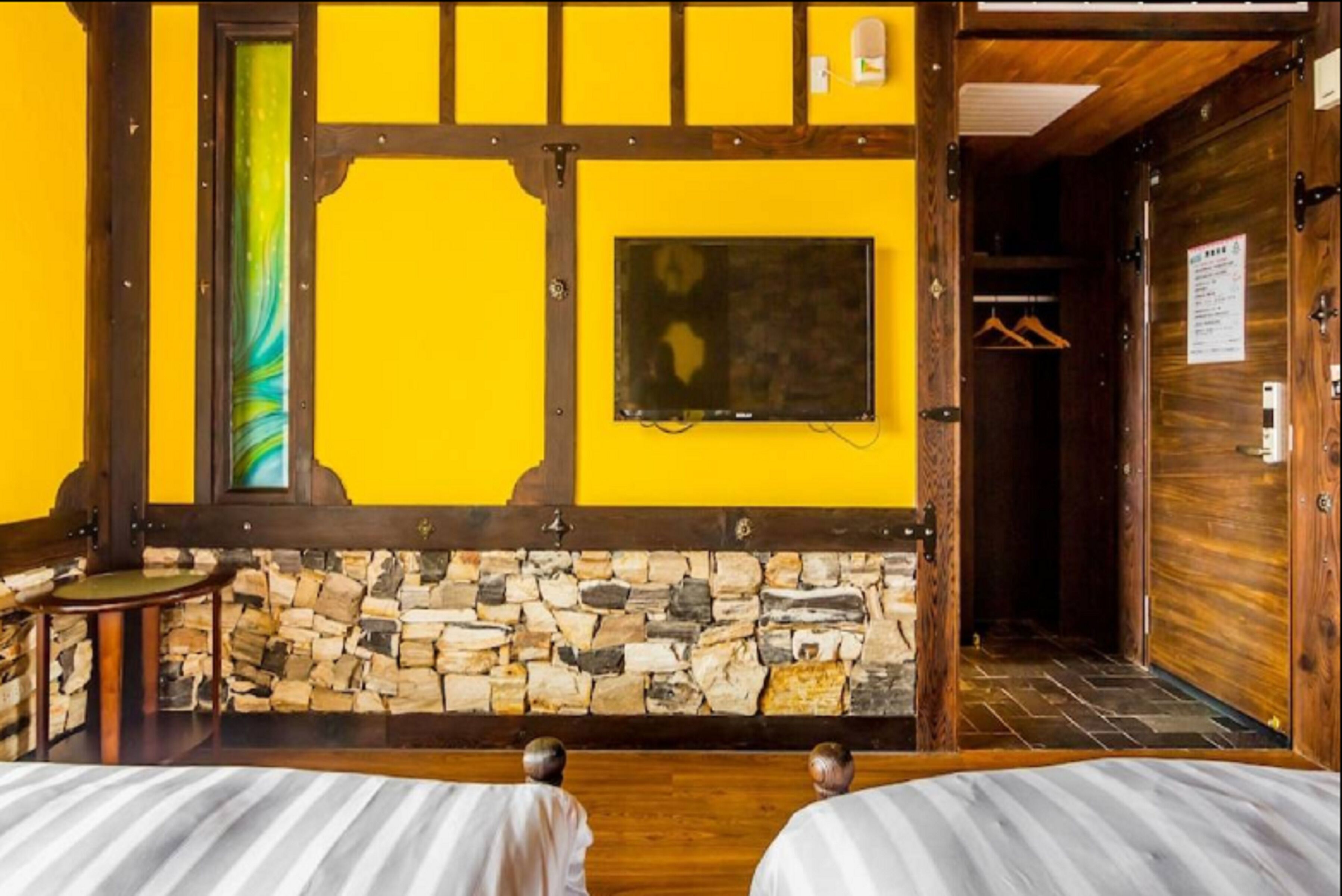 Una habitación con pared de piedra, vigas de madera, una cama, una mesita y un perchero.
