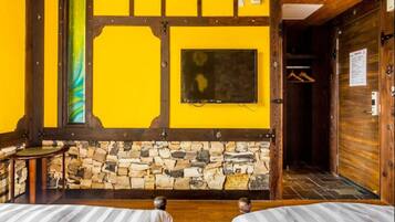 A room with a stone wall, wooden beams, a bed, a small table, and a coat rack.