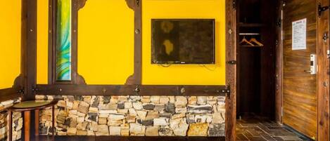 Una habitación con pared de piedra, vigas de madera, una cama, una mesita y un perchero.