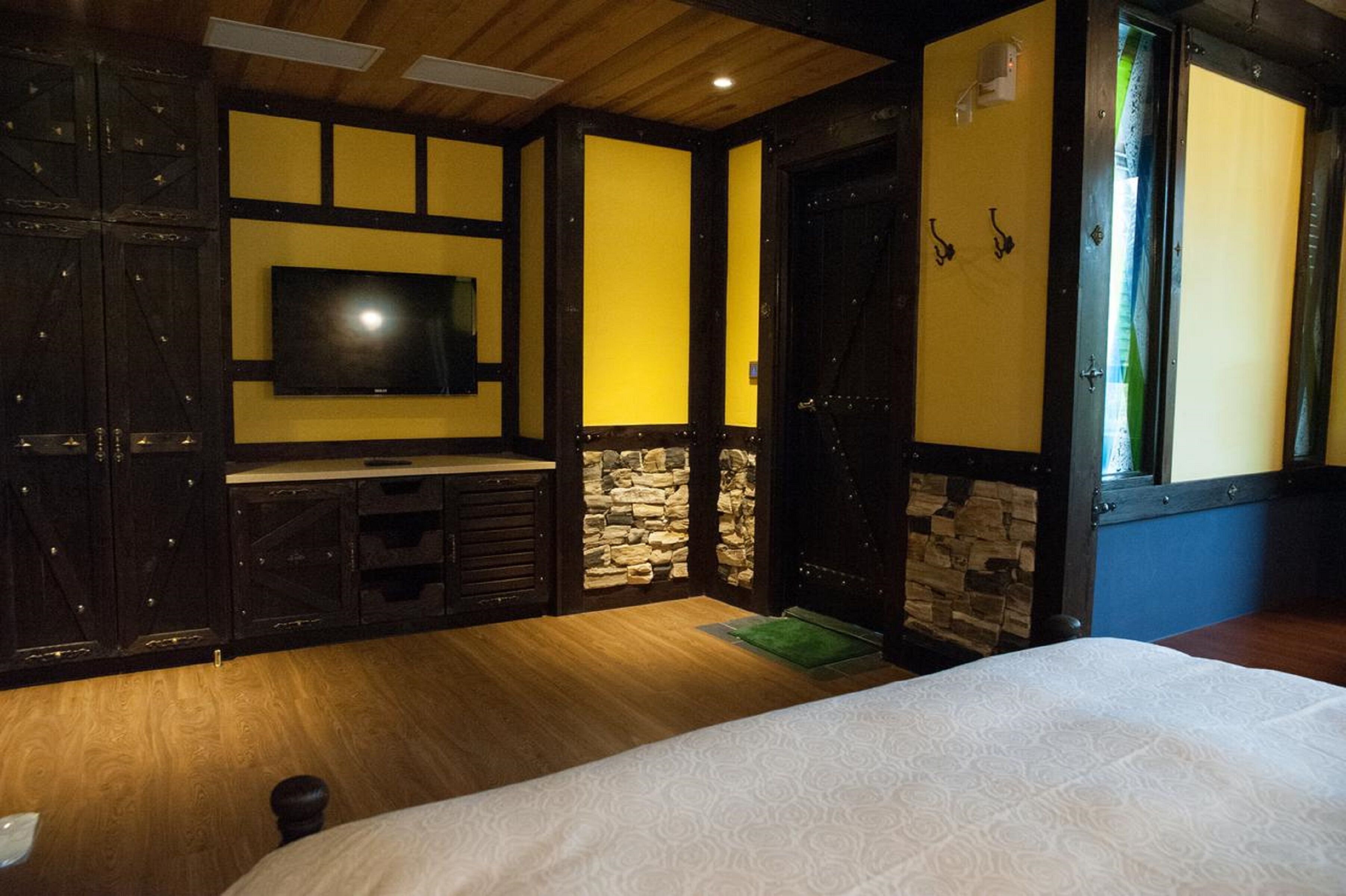Een slaapkamer met een bed, een aan de muur bevestigde televisie, houten kasten en een stenen muur.
