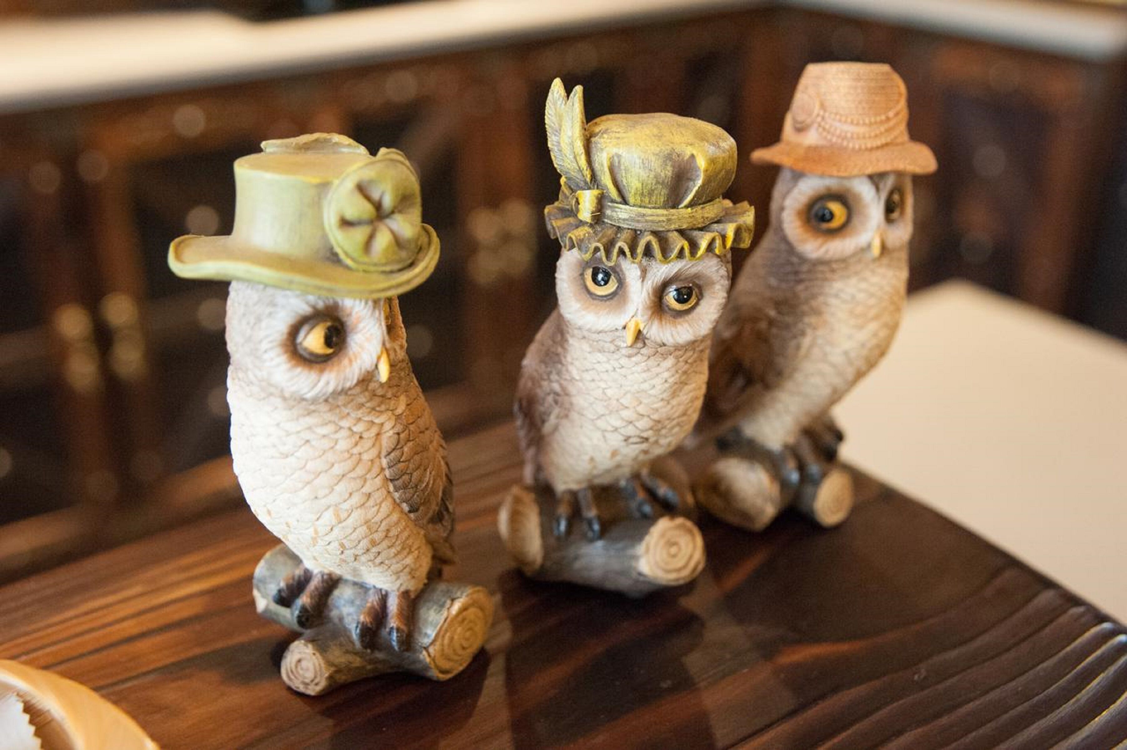 Tres figuras de búhos con sombreros sobre una superficie de madera.