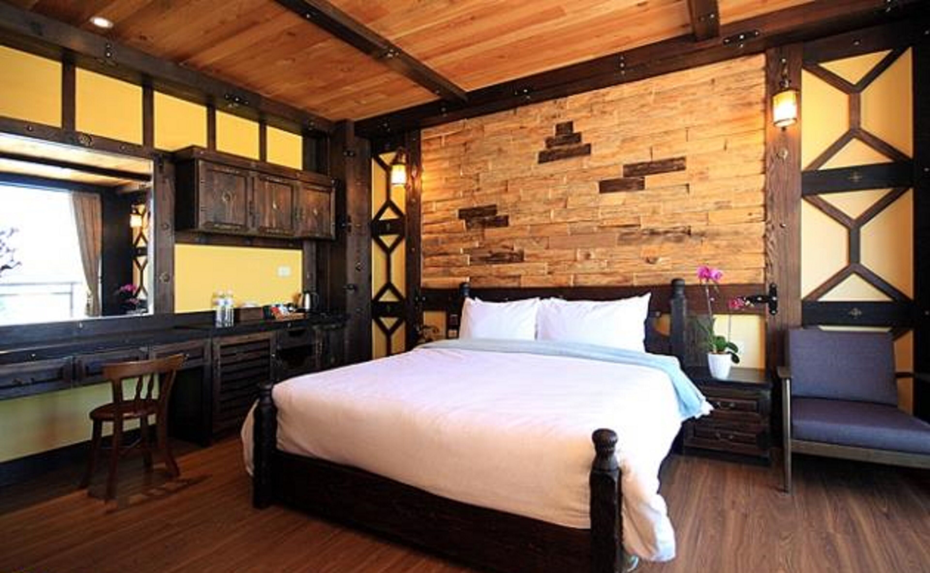A room with a wooden ceiling, a bed with white bedding, a wooden desk, and a chair.