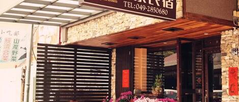 A hotel entrance with a wooden overhang, stone facade, and a signboard with contact information.