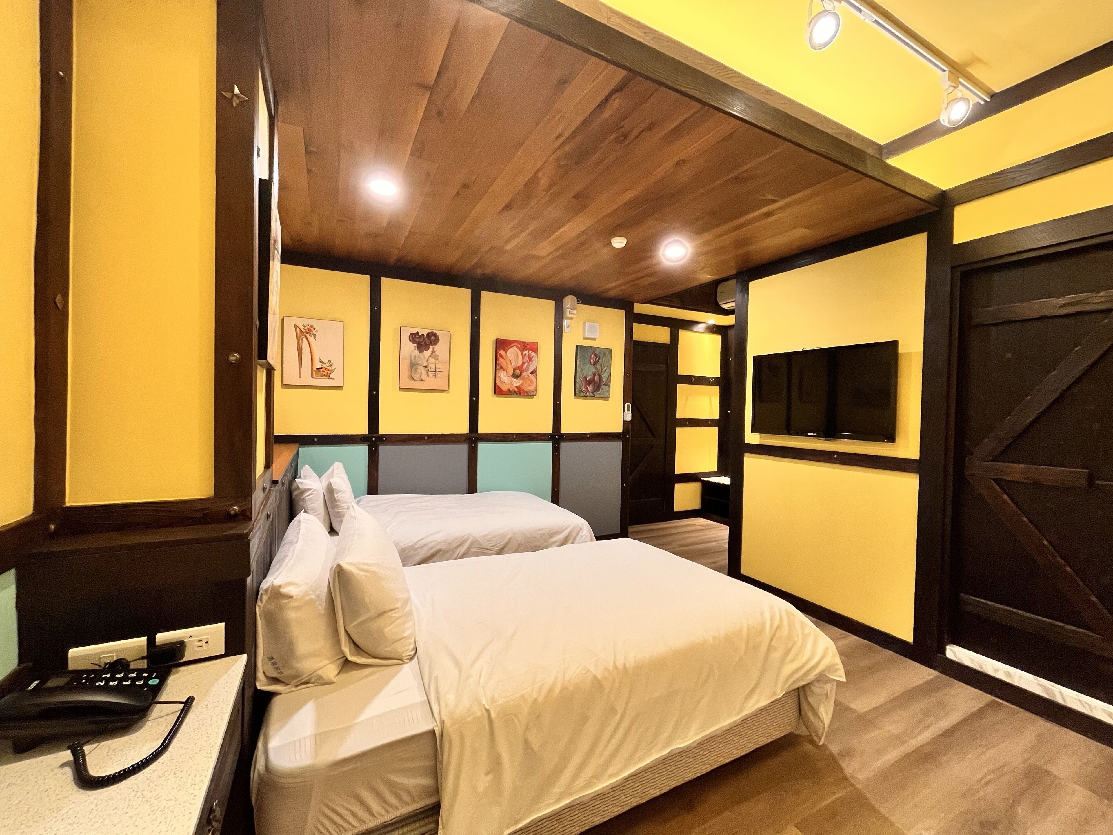 A hotel room with two beds, a desk with a telephone, and artwork on the walls.