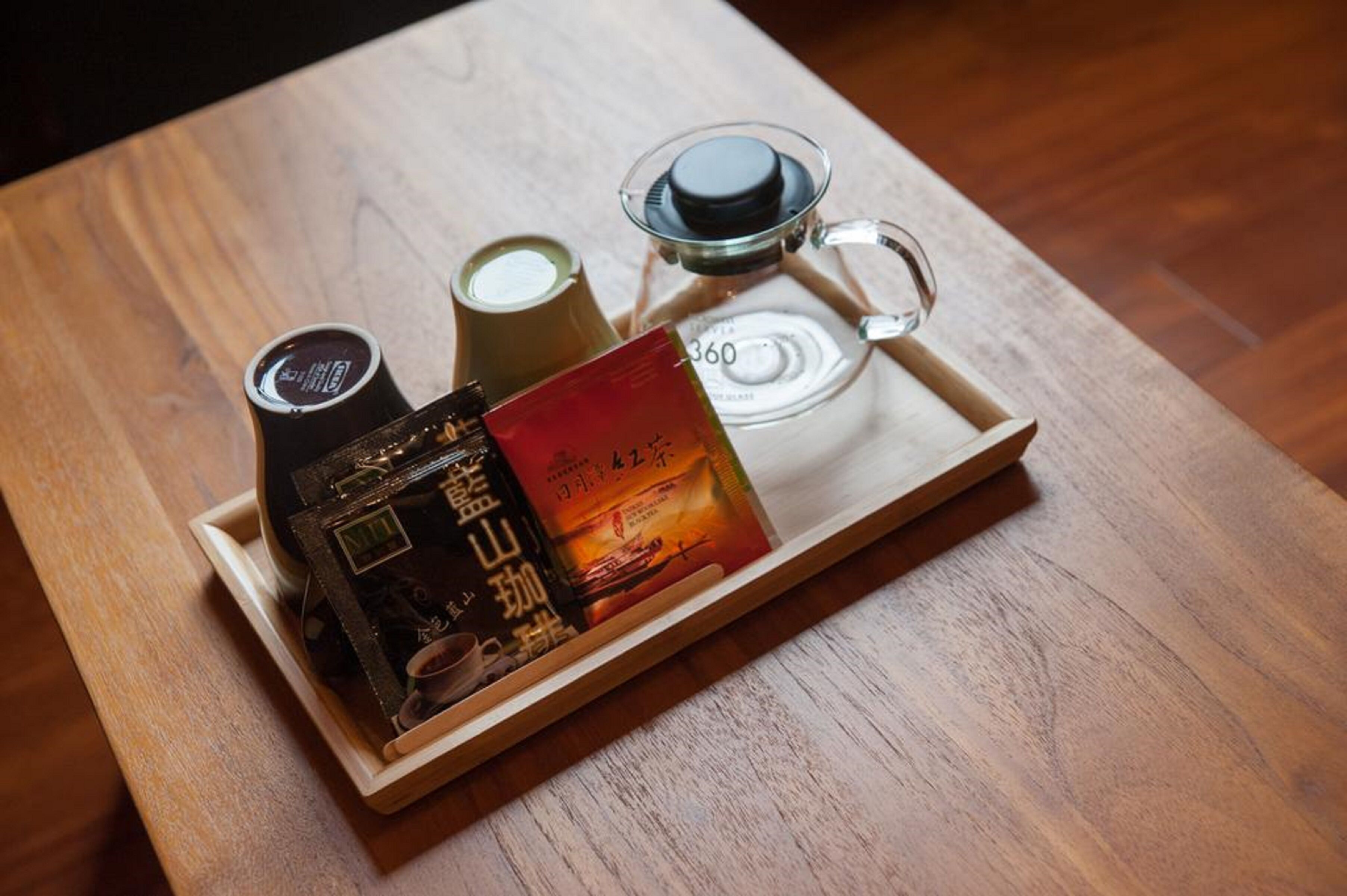 A tray with a coffee maker, a glass of milk, and a book on a wooden table.