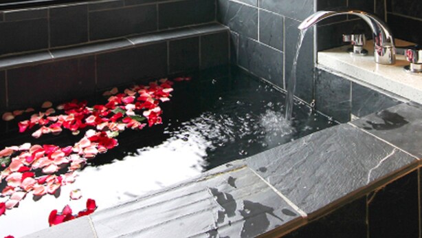 A bathroom with a large window, a bathtub with rose petals, and a view of the sea.