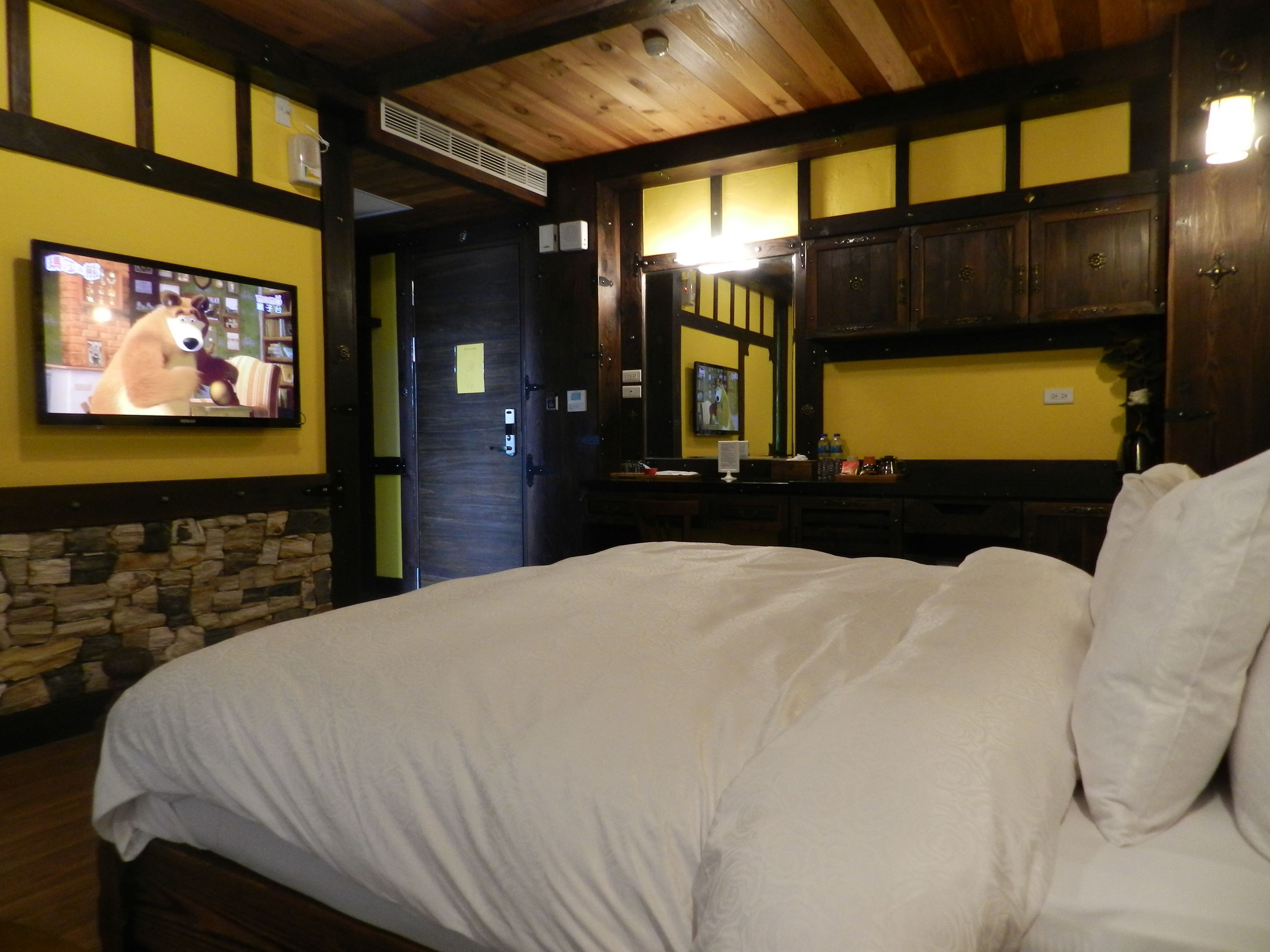 Una habitación de hotel con una cama grande, un televisor montado en la pared y paneles de madera.