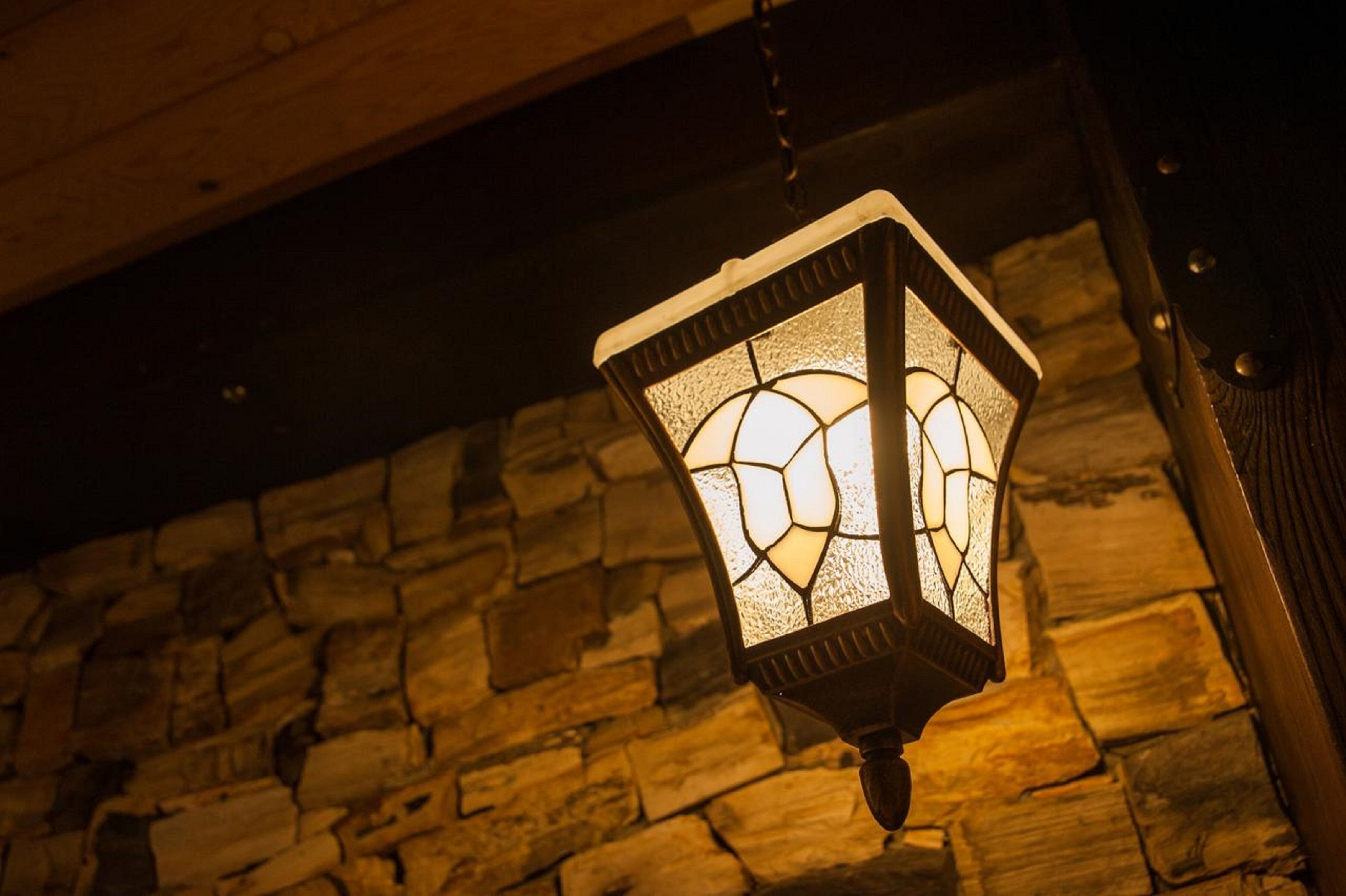A hanging lantern with a stained glass design, mounted on a stone wall.