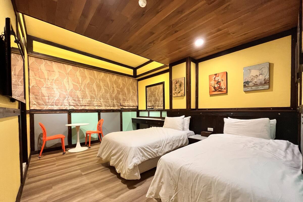 Habitación de hotel con dos camas, una mesita y una silla.
