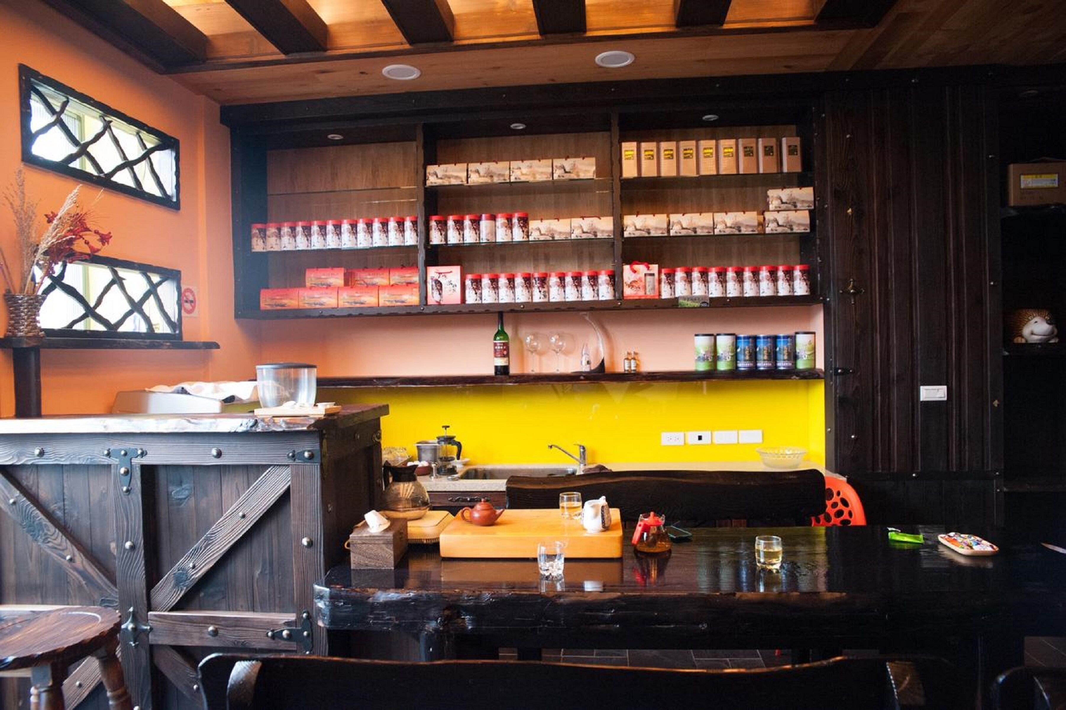 Un restaurante con barra de madera, estantes con condimentos y una pared de acento amarilla.