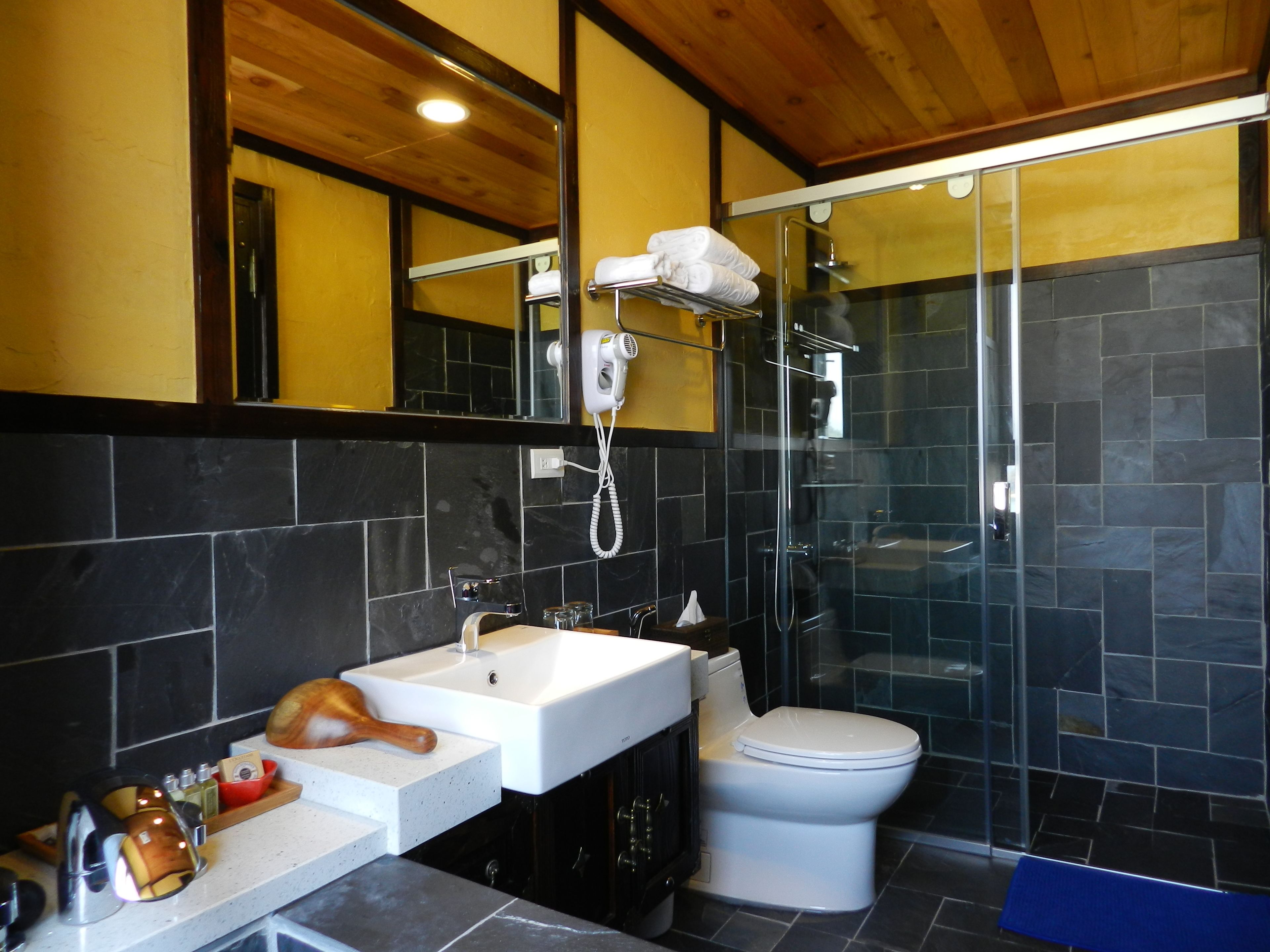 A modern bathroom with a white sink, a toilet, a glass shower enclosure, and a hairdryer mounted on the wall.