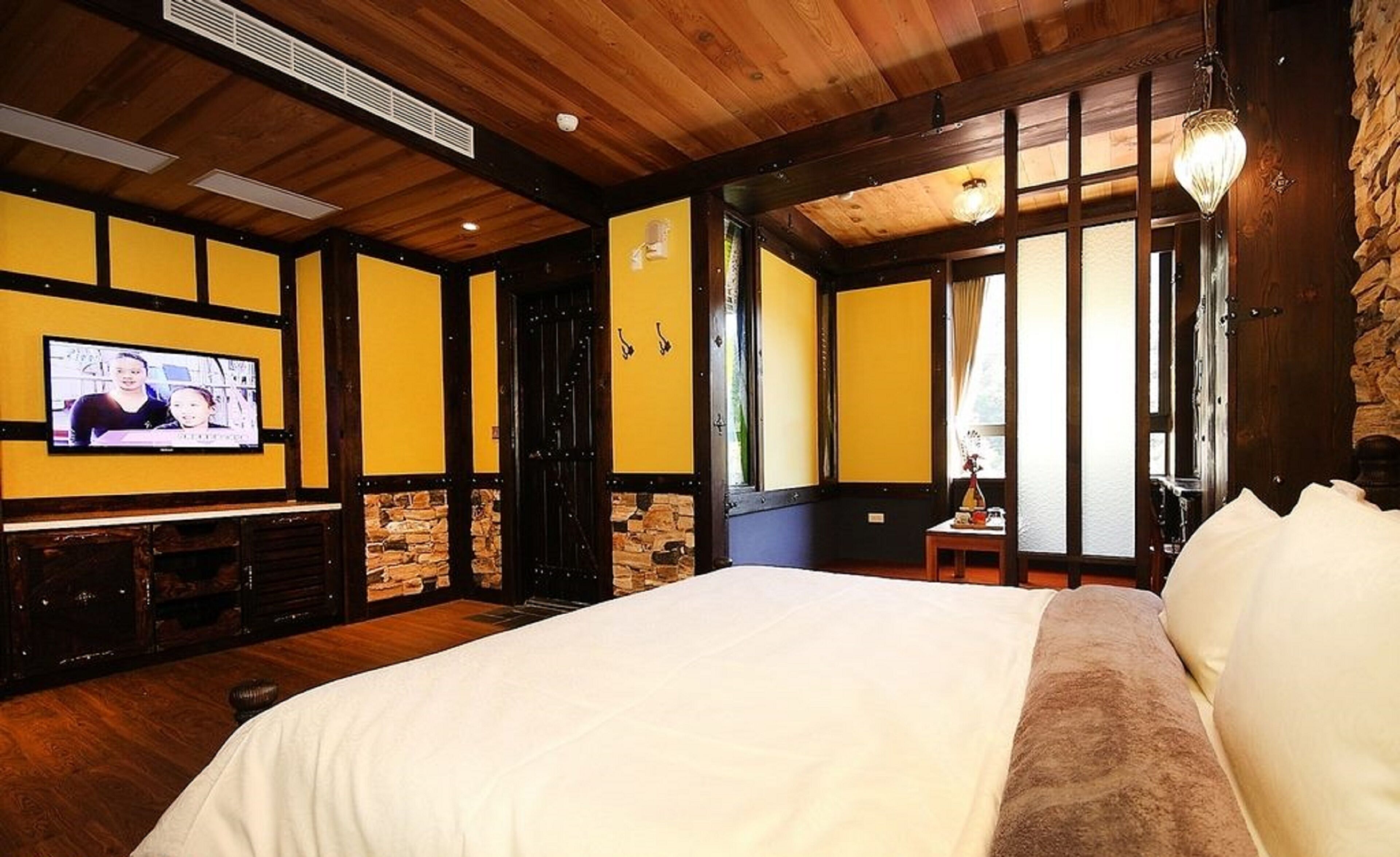 Una habitación de hotel con una cama grande, techo de madera, pared de piedra y un televisor en la pared.