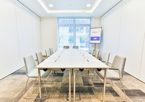 A conference room with a long table, chairs, a whiteboard, and a window with blinds.