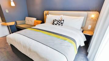 A hotel room with a bed, a chair, a nightstand, and a lamp.