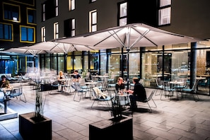 Een terras met tafels en stoelen, grote parasols en uitzicht op de straat.