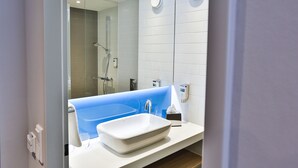 A modern bathroom with a white sink, a blue bathtub, and a glass shower enclosure.