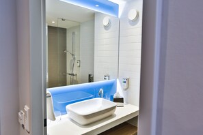 Un baño moderno con un lavamanos blanco, una bañera azul y un recinto de ducha de vidrio.