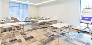 Un salón de conferencias con varias mesas y sillas, una pizarra en la pared y una ventana con persianas.
