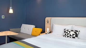 A hotel room with a bed, a bedside table, a lamp, and a wall-mounted phone.