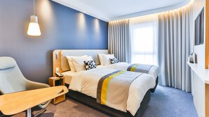 A hotel room with a large bed, a desk, a chair, and a TV.