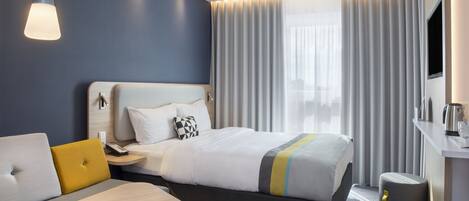 Una habitación de hotel moderna con una cama bien hecha, una mesita de noche, un escritorio pequeño y una silla.