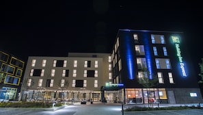 Un hotel Holiday Inn Express con diseño moderno, que presenta una entrada bien iluminada y un área de estar al aire libre.