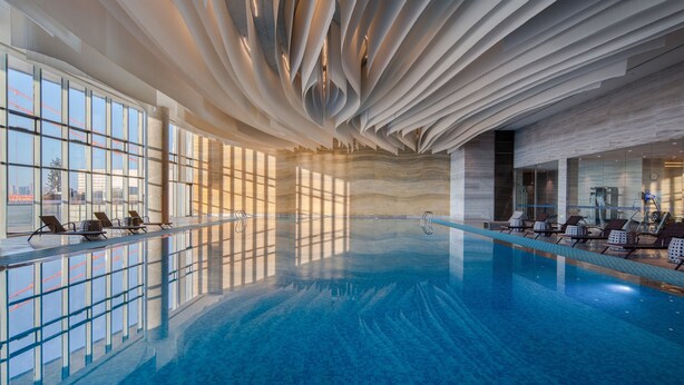 An indoor swimming pool with a modern ceiling design, large windows, and sun loungers. - Hilton Wuhan Riverside (Wuhan)