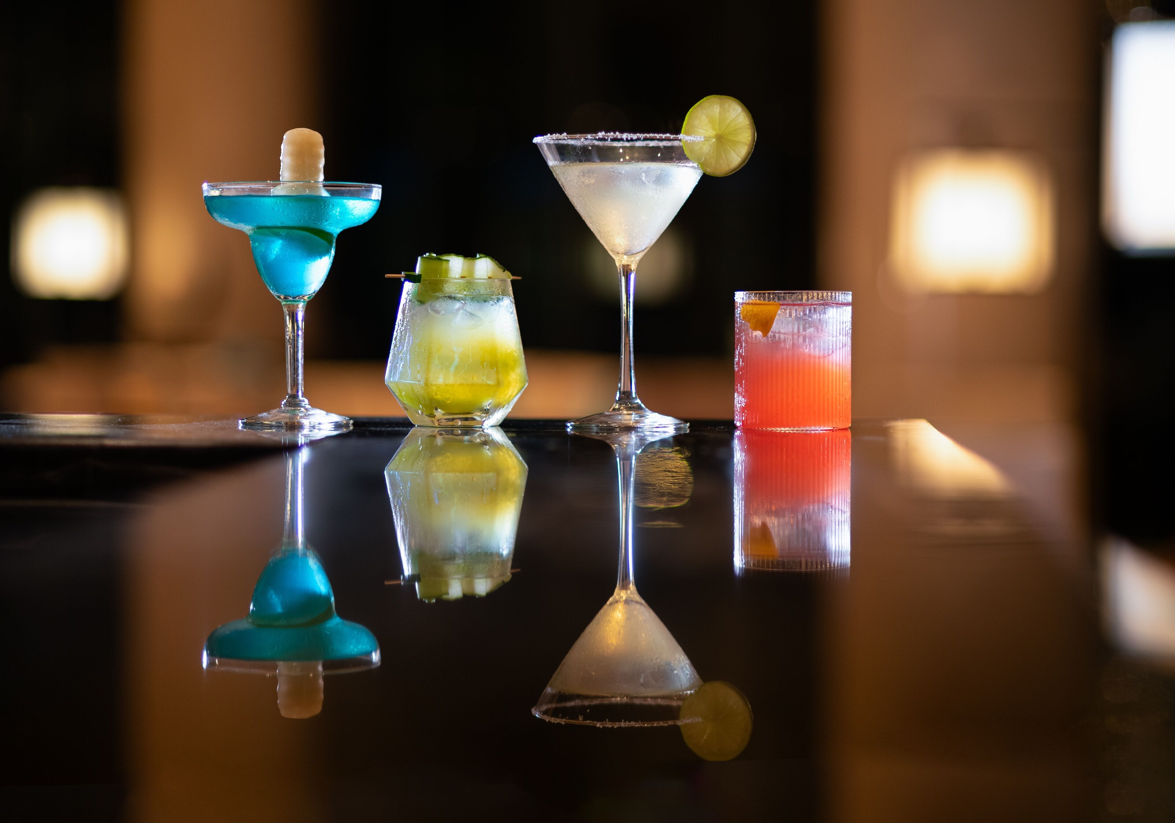 Cuatro cócteles diferentes sobre una superficie de bar reflectante.
