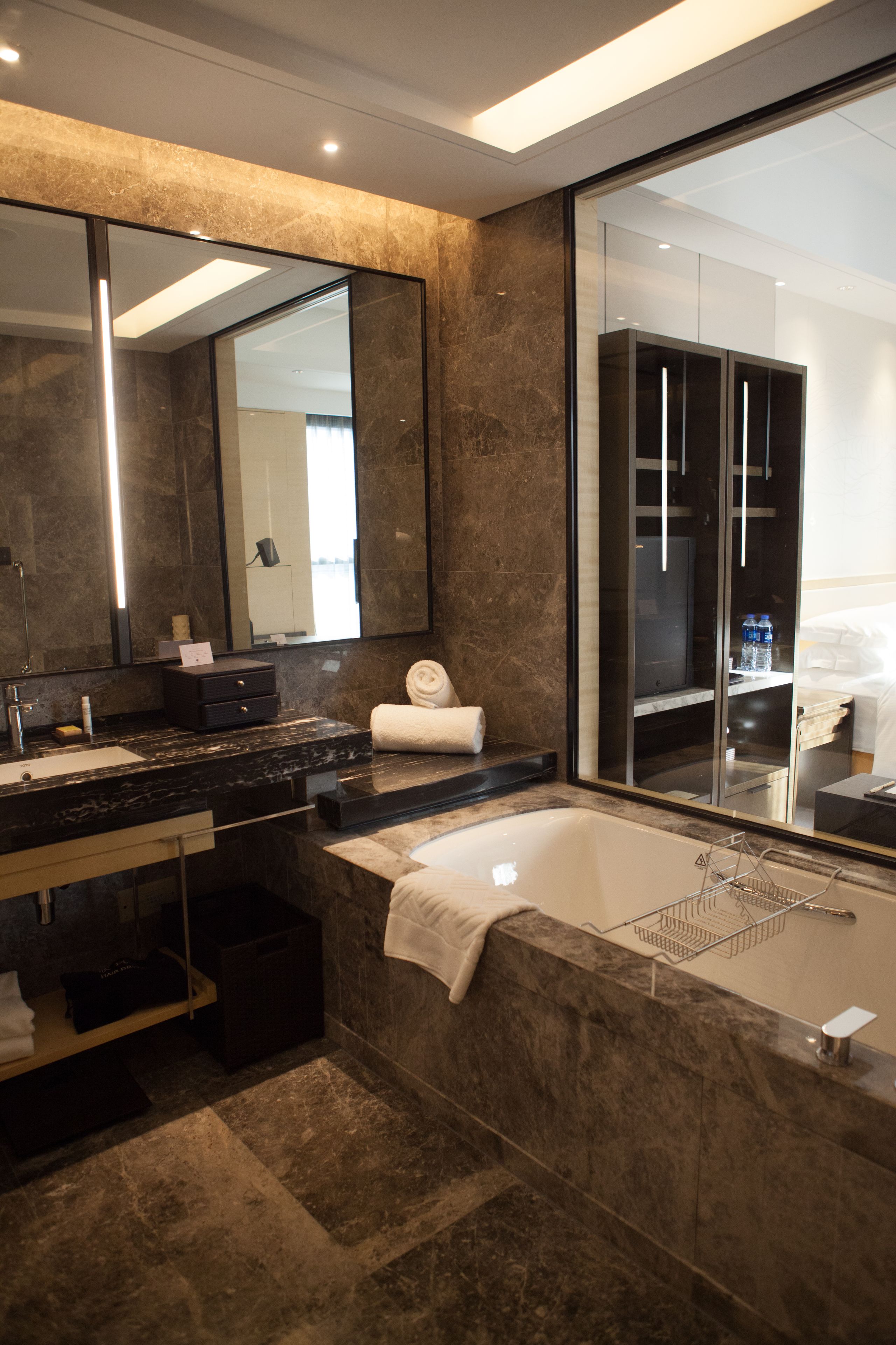 A modern bathroom with a marble sink, a large mirror, a bathtub, and a walk-in closet.