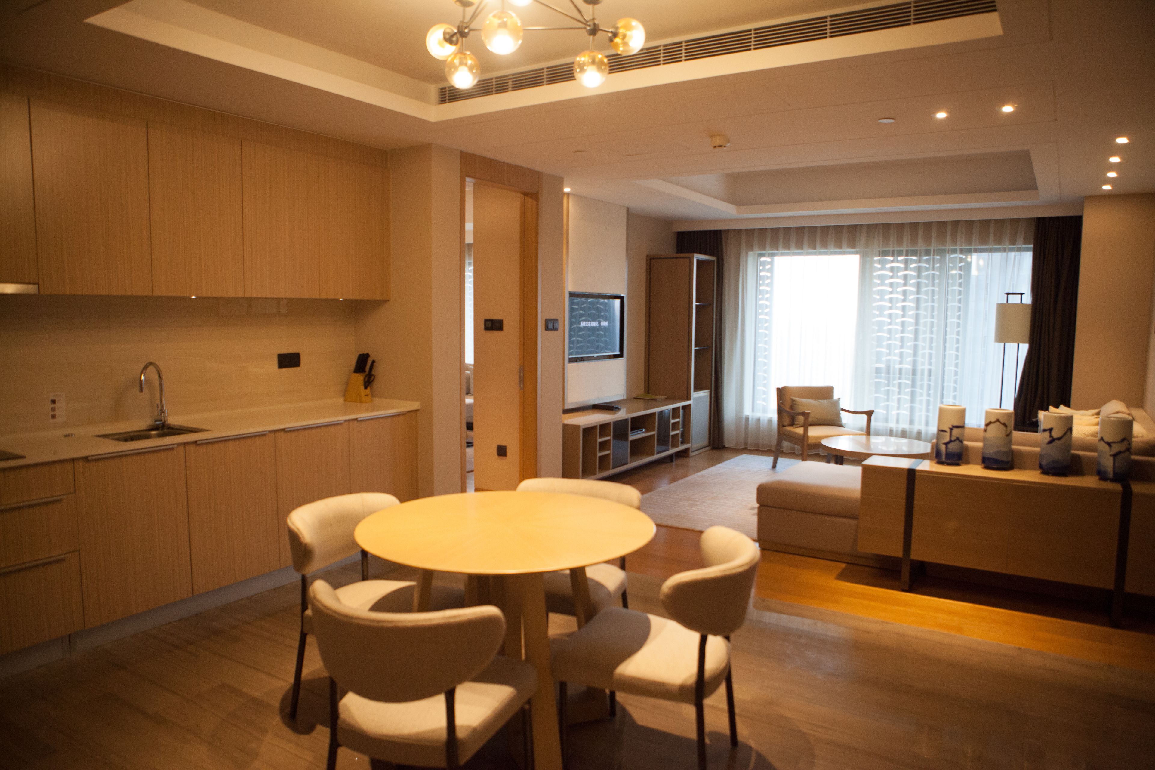 Una habitación de hotel moderna con comedor, kitchenette y zona de estar con sofá y sillones.