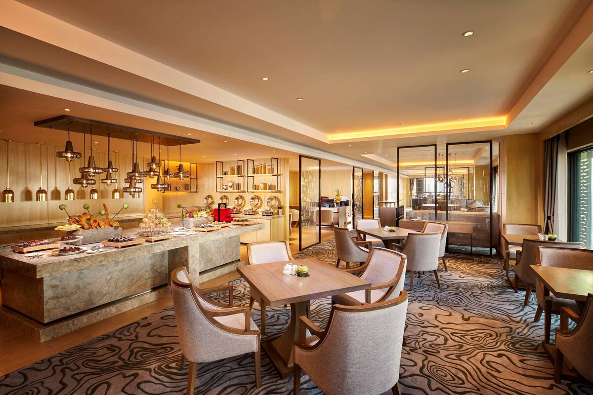 A modern hotel lobby with a marble reception desk, seating area, and a view of the dining area.