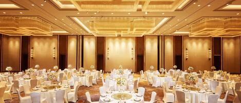 Un amplio salón de banquetes con mesas redondas dispuestas para comer, cada una con manteles blancos y sillas, y centros de mesa con flores.