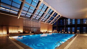 An indoor swimming pool with a glass ceiling, lounge chairs, and a well-lit interior. - Hilton Suzhou (Suzhou)