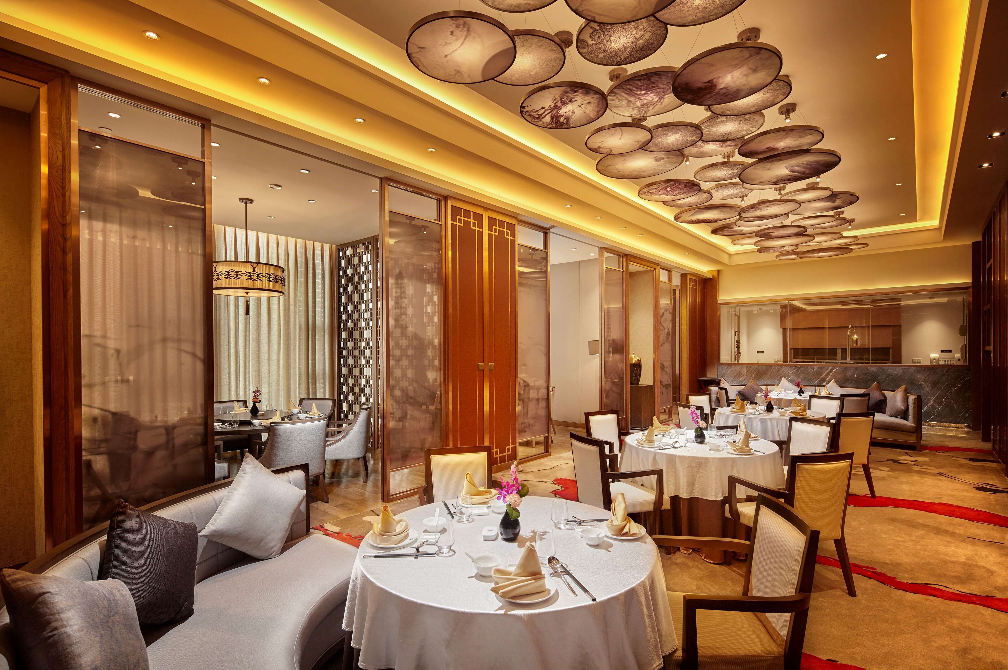 A hotel dining area with round tables set for a meal, a sofa with cushions, and a decorative ceiling with circular elements.