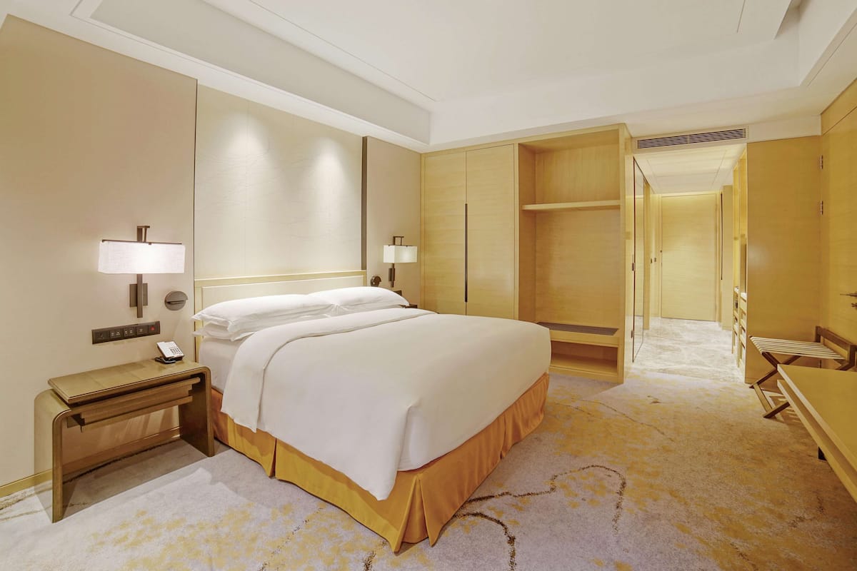 A hotel room with a large bed, bedside lamps, a desk with a telephone, and a wardrobe.