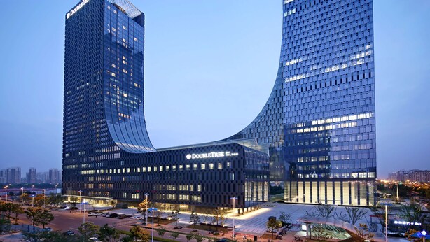 A modern, curved skyscraper with a glass facade, likely a hotel or office building, surrounded by a well-lit urban area. - Hilton Suzhou (Suzhou)
