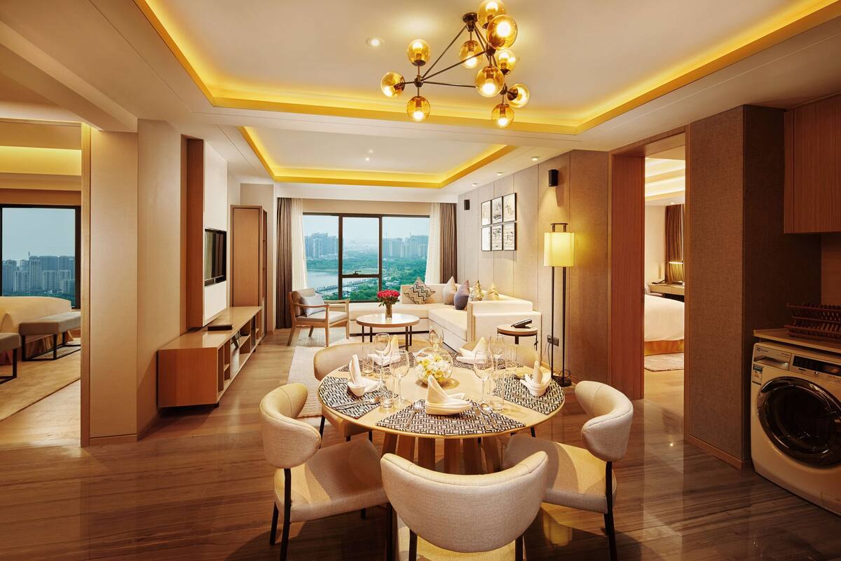 A modern hotel room with a dining area, a sofa set, a TV, and a washing machine.