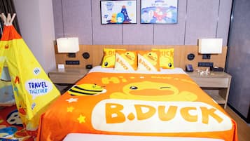 Une chambre d’hôtel avec un lit agrémenté d’une couvre-lit aux motifs de B. Duck, une table de chevet avec une lampe, une horloge murale et un tableau encadré au-dessus du lit.