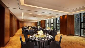 A spacious banquet hall with round tables set for dining, large windows offering views, and a wooden floor.