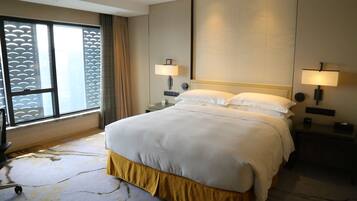 A hotel room with a large bed, two bedside lamps, a window with a view, and a carpeted floor.