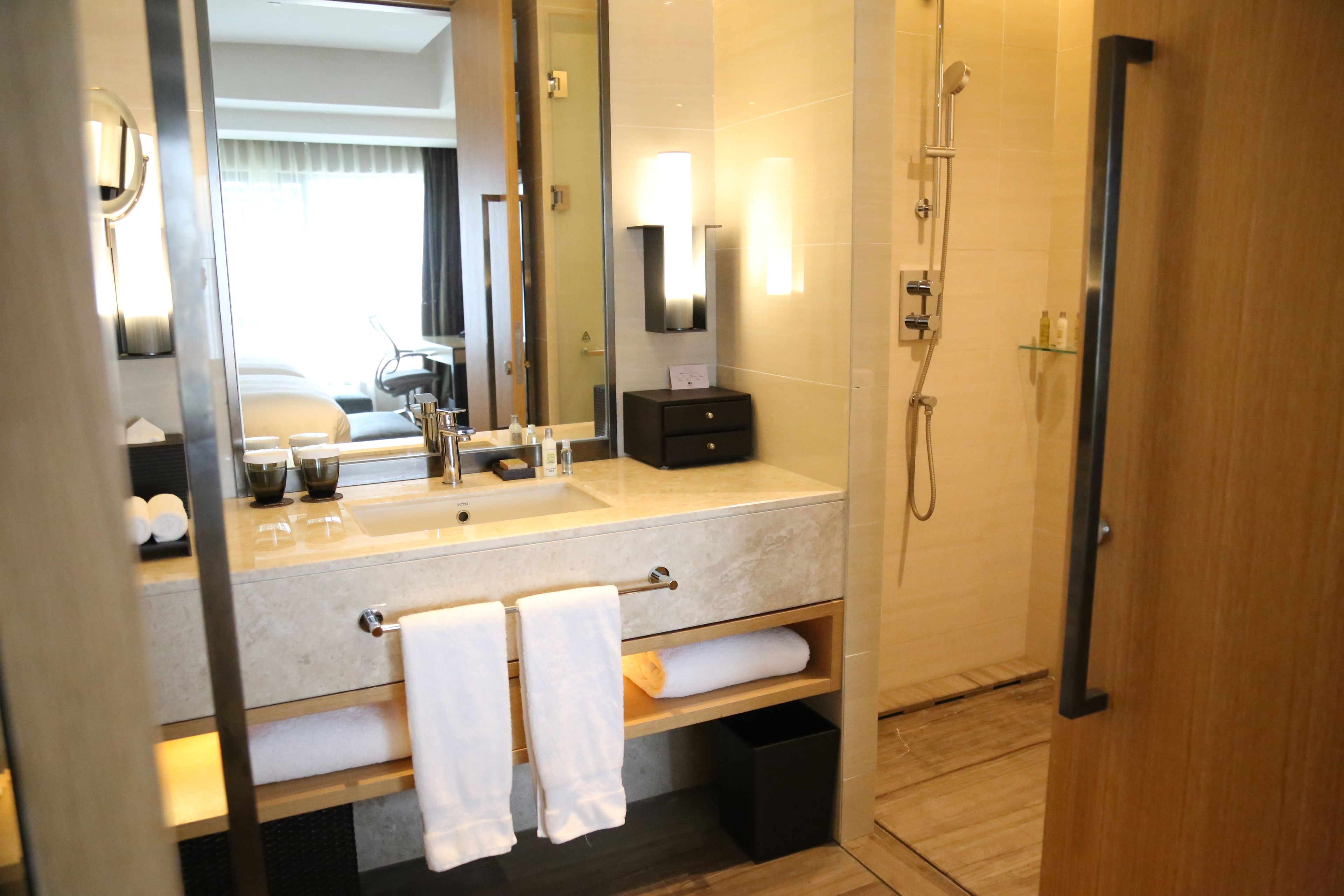 Une salle de bain moderne avec un grand miroir, un lavabo doté d’un porte-serviettes, une douche et une porte en bois.