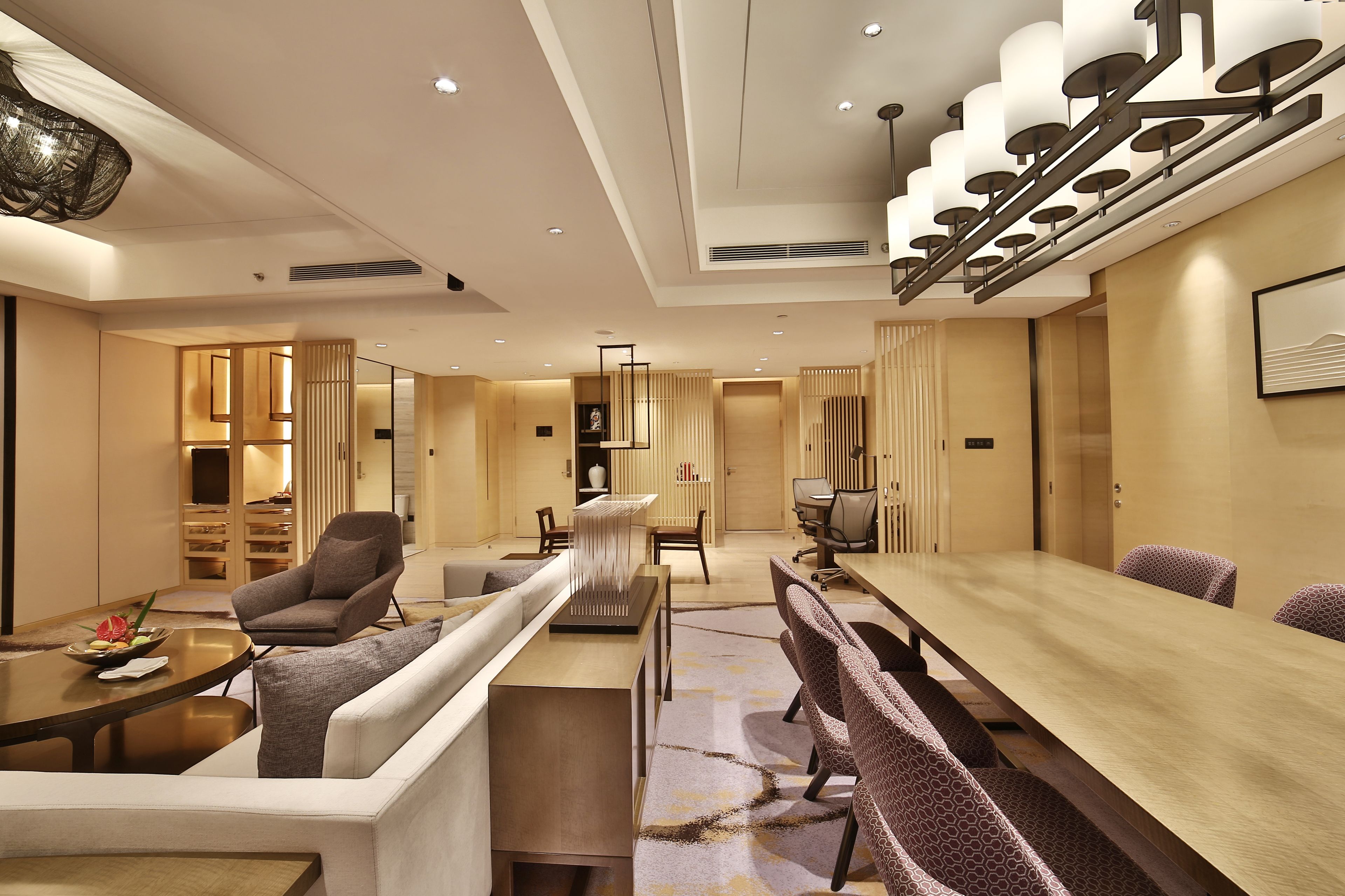 A modern hotel lobby with a long dining table, comfortable seating, and a decorative staircase.
